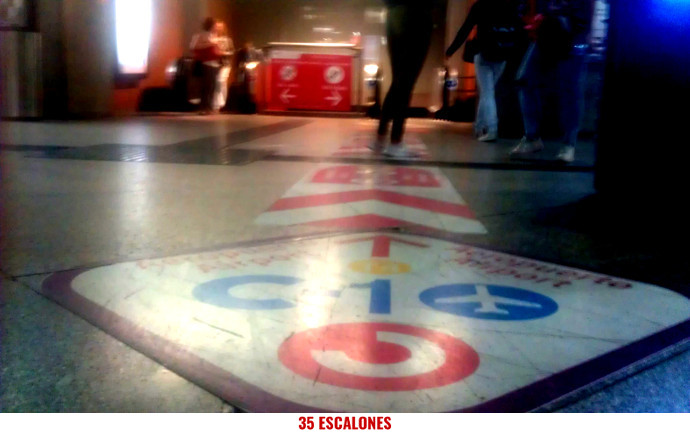 Foto de señales apuntando hacia escaleras mecánicas para bajar al Andén 1 desde el vestíbulo de la Estación de Atocha-Cercanías-Renfe